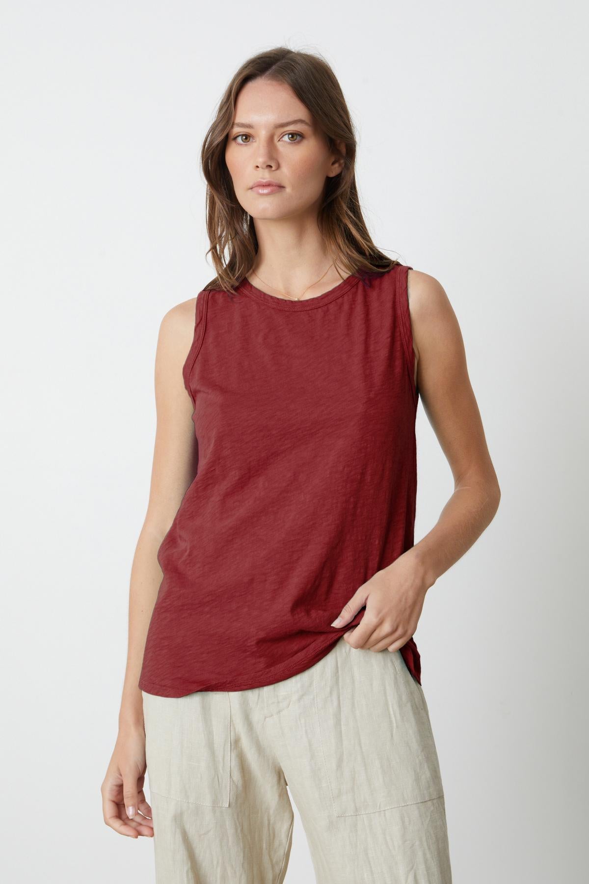   A woman in a burgundy TAURUS COTTON SLUB TANK by Velvet by Graham & Spencer and beige pants, styled in a crew-neck shirt. 