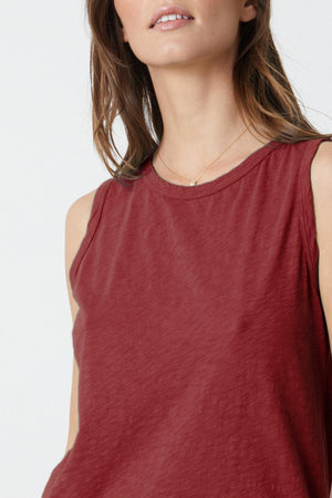 Person wearing a tomboy-inspired, sleeveless, red TAURUS COTTON SLUB TANK by Velvet by Graham & Spencer and a thin gold necklace. Their loose hair cascades naturally as the image captures them from shoulders up.