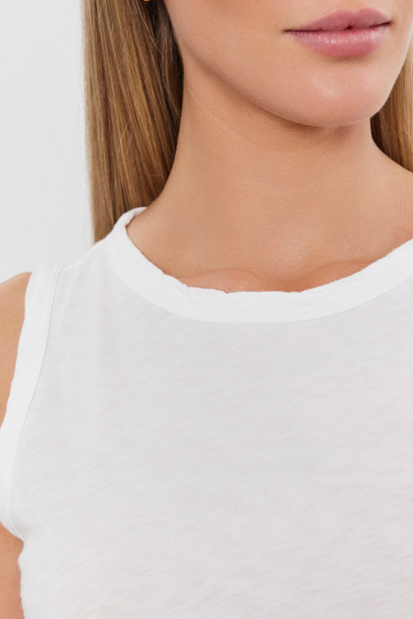 Person wearing a sleeveless white shirt stands against a plain background. The image shows the lower half of their face and upper body, highlighting the textured cotton slub of the Velvet by Graham & Spencer TAURUS TANK TOP—a versatile staple for any wardrobe.