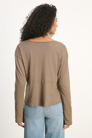 Woman with curly hair wears the Velvet by Graham & Spencer VINT TEE in brown, styled with light blue jeans. She is shown from the back against a plain light background.