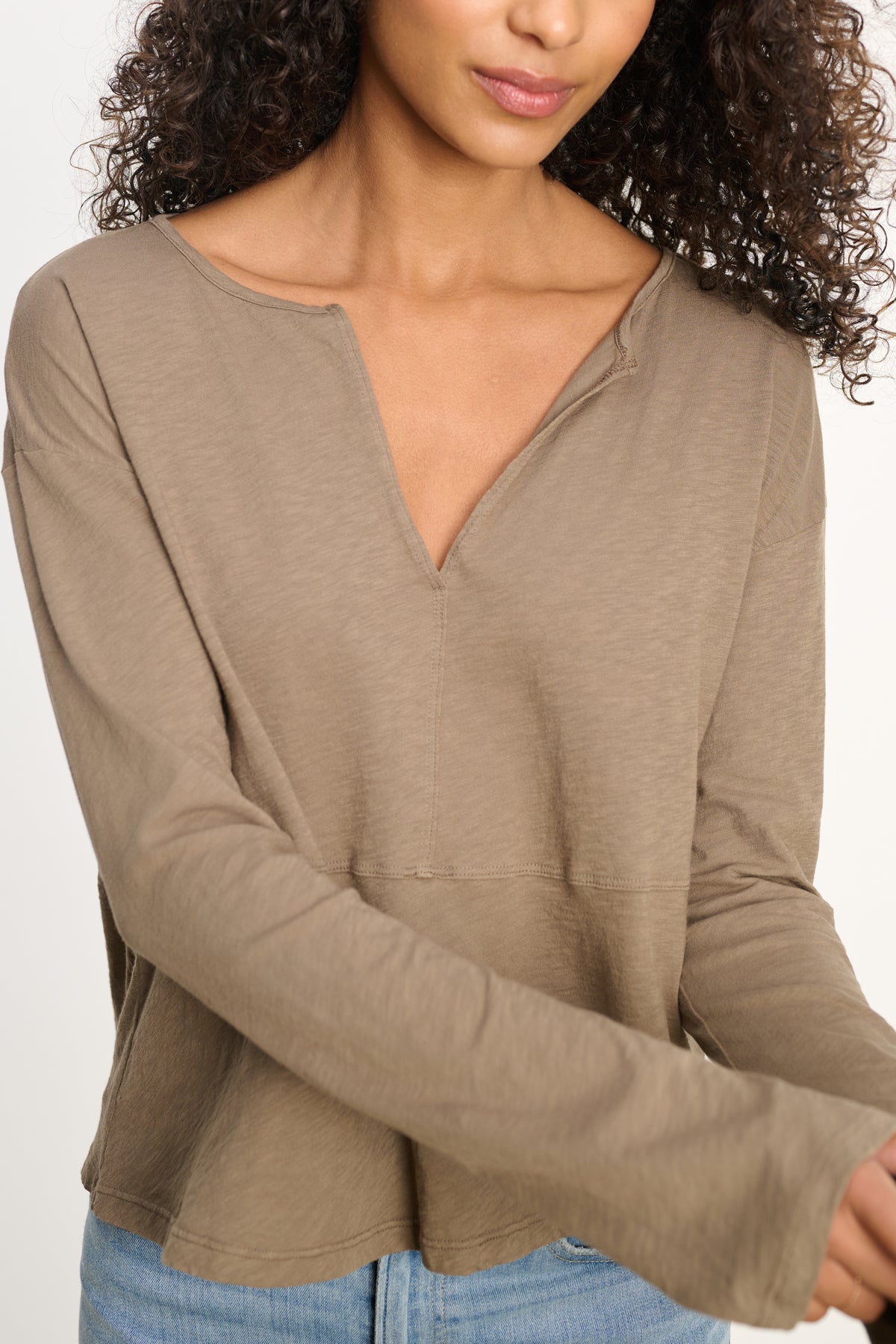 A woman wears the VINT TEE by Velvet by Graham & Spencer—a relaxed fit, long sleeve beige vintage cotton slub tee with a V-notch neckline—paired with light blue jeans, standing against a plain background.-Hover Image