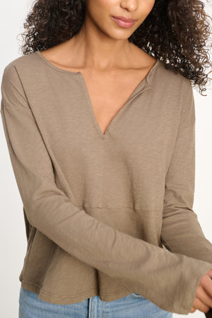 A woman wears the VINT TEE by Velvet by Graham & Spencer—a relaxed fit, long sleeve beige vintage cotton slub tee with a V-notch neckline—paired with light blue jeans, standing against a plain background.