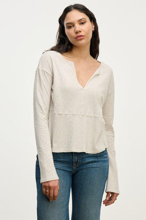 A woman wearing the Velvet by Graham & Spencer VINT TEE, a vintage cotton slub long sleeve top in light beige, paired with blue jeans, stands against a plain white background.