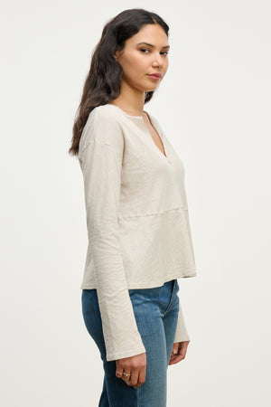 A woman with long dark hair wears the Velvet by Graham & Spencer VINT TEE—a relaxed fit vintage cotton slub long sleeve tee—with blue jeans, standing sideways against a plain white background.