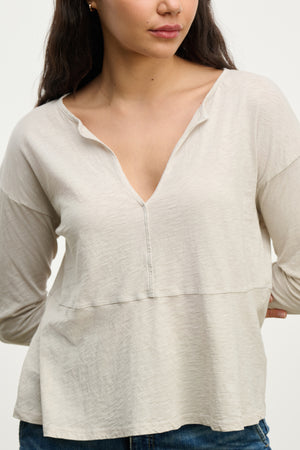 A woman wears the Velvet by Graham & Spencer VINT TEE, a vintage cotton slub long sleeve with a relaxed fit, paired with blue jeans, standing against a plain background with one hand behind her back.