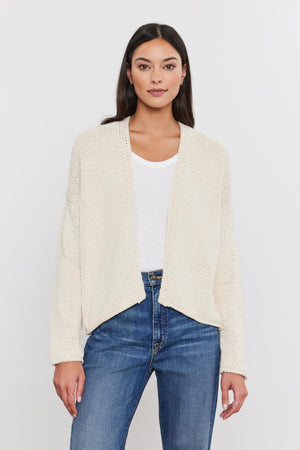 Woman in a Velvet by Graham & Spencer HOLLIE CARDIGAN, white t-shirt, and blue jeans standing against a plain background.