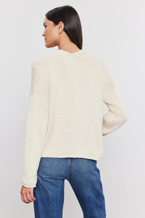 Woman standing with her back to the camera, wearing a cream knitted HOLLIE CARDIGAN from Velvet by Graham & Spencer and blue jeans.