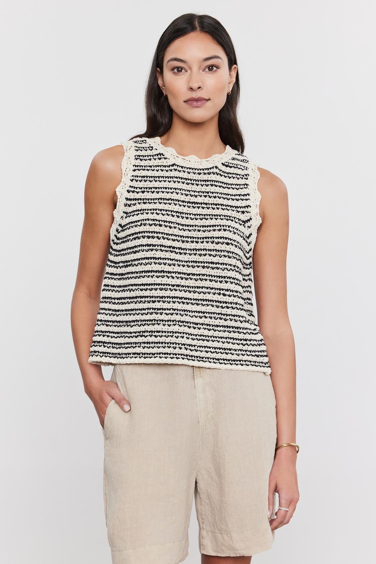 A woman wearing a Velvet by Graham & Spencer SOPHIE SWEATER VEST with scallop details and beige trousers, standing against a white background.-36910013677761