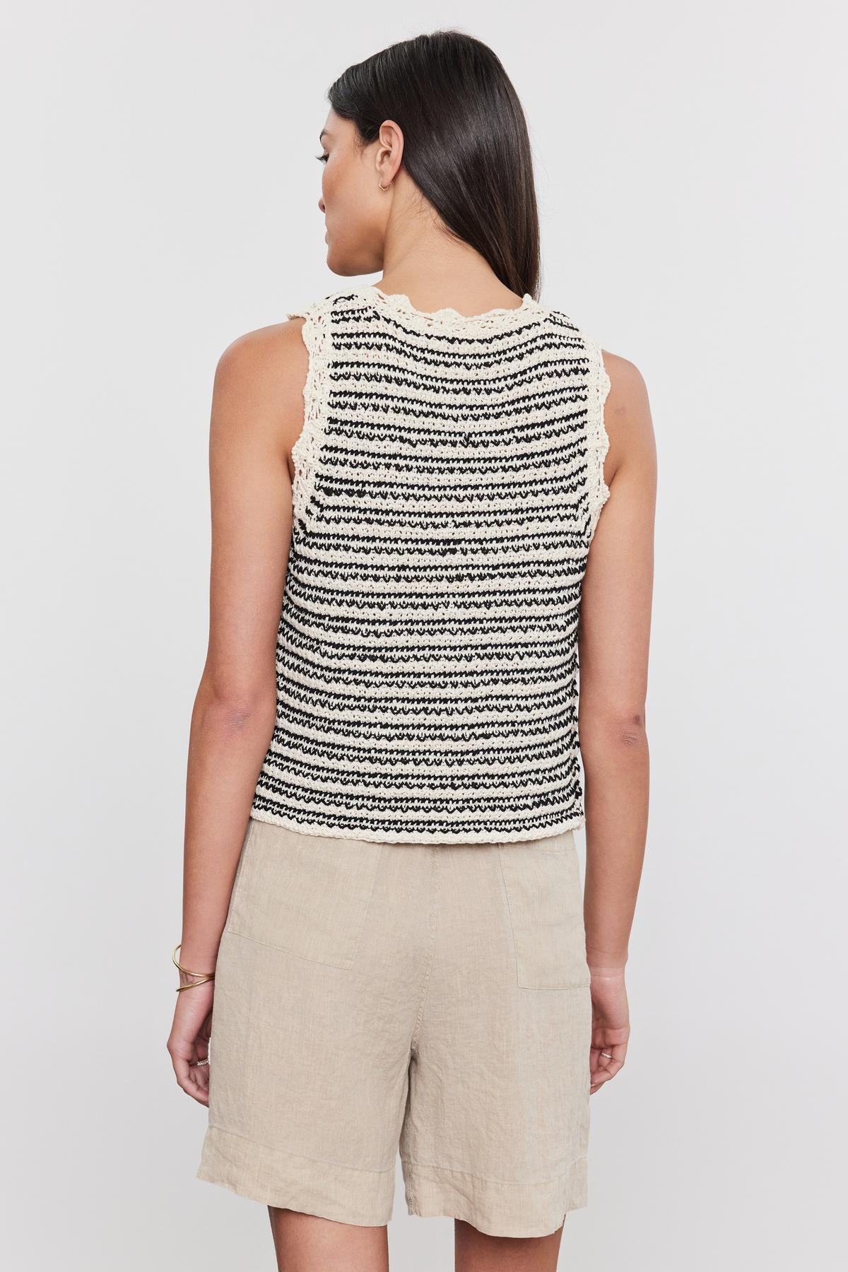 Woman standing with her back to the camera, wearing a black and white striped SOPHIE SWEATER VEST sleeveless top with a crew neckline and beige shorts by Velvet by Graham & Spencer.-36910013743297
