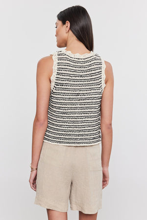Woman standing with her back to the camera, wearing a black and white striped SOPHIE SWEATER VEST sleeveless top with a crew neckline and beige shorts by Velvet by Graham & Spencer.