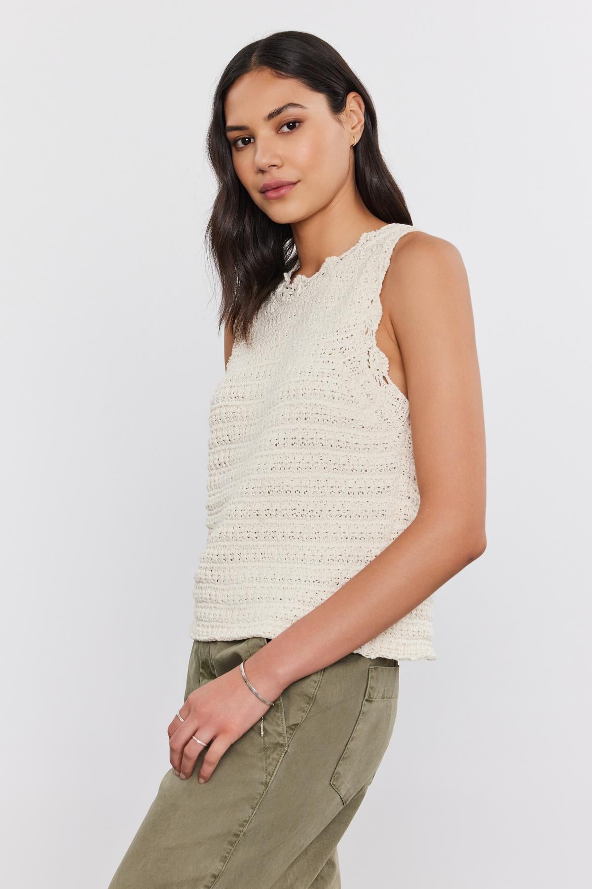   A woman with long dark hair wears an off-white Velvet by Graham & Spencer SOPHIE SWEATER VEST featuring scallop details and olive green pants, posing against a plain white background. 