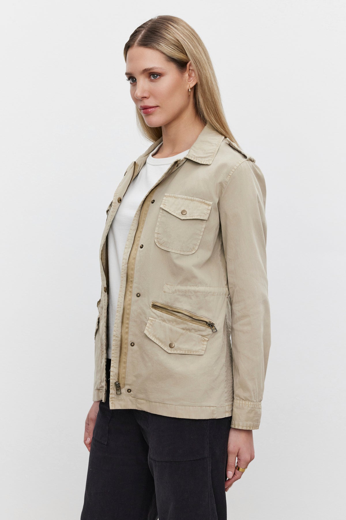   A person is wearing the RUBY LIGHT-WEIGHT ARMY JACKET by Velvet by Graham & Spencer, made from cotton twill in a beige color, featuring multiple pockets for enhanced versatility, layered over a white shirt against a plain white background. 