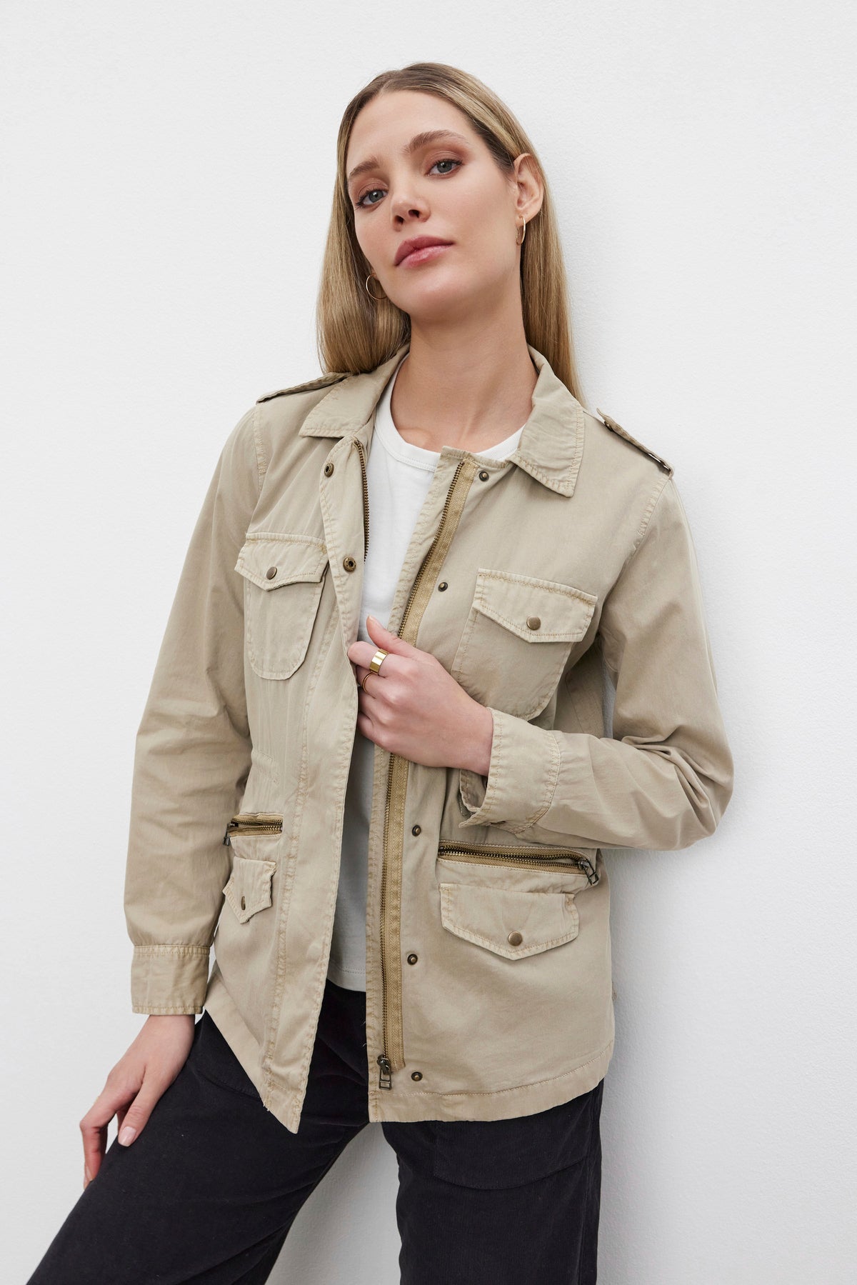   A person is standing against a white background wearing the RUBY LIGHT-WEIGHT ARMY JACKET by Velvet by Graham & Spencer, crafted from beige cotton twill and featuring practical pockets, over a white shirt. 