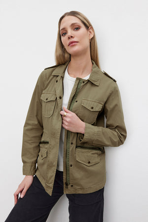 A person with long blonde hair wears the RUBY LIGHT-WEIGHT ARMY JACKET by Velvet by Graham & Spencer, crafted from olive green cotton twill, over a white shirt. They exude off-duty glamour while posing against a plain white background.