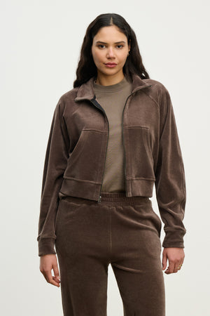 A woman faces forward against a light background, wearing the CLAIRE JACKET by Velvet by Graham & Spencer—a brown cotton velour hoodie—paired with matching pants over a taupe shirt.