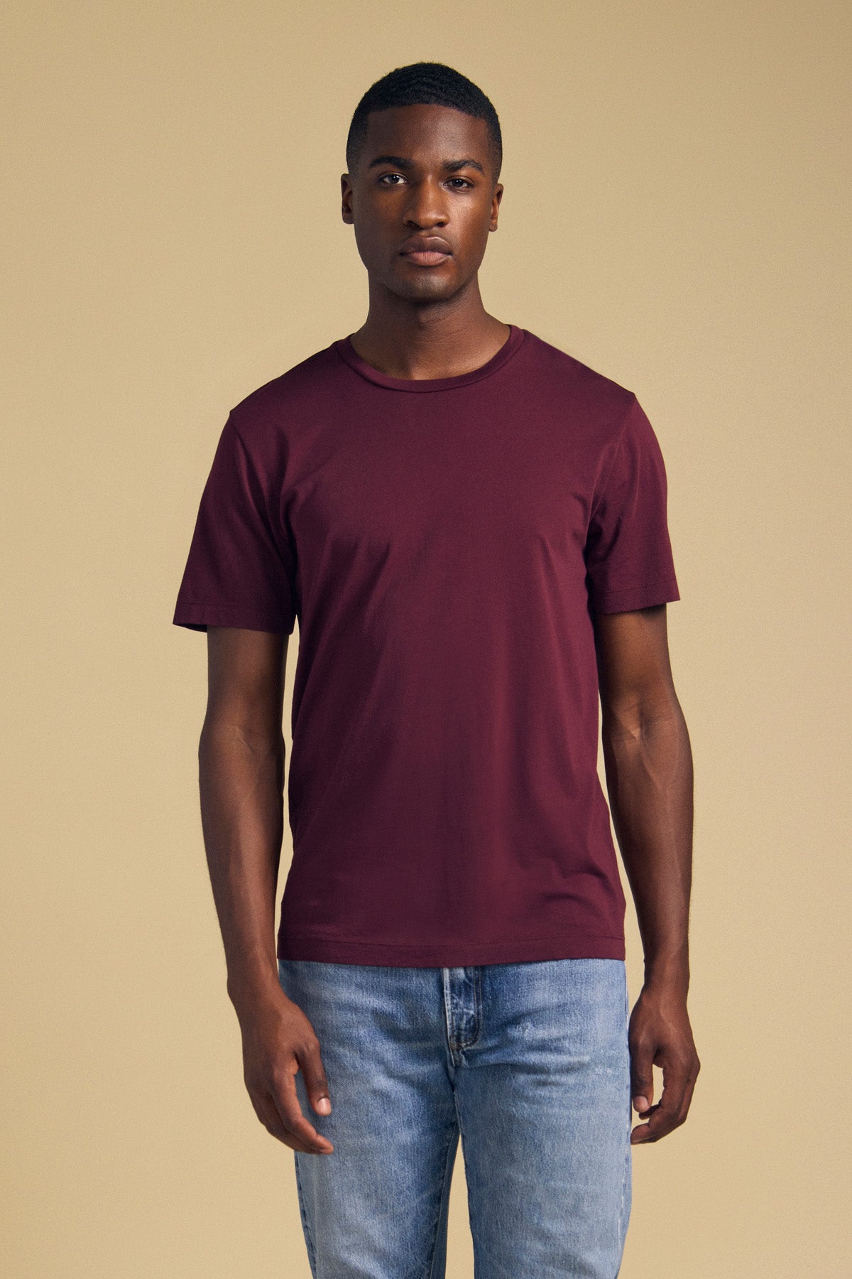 Front view of a dark plum short-sleeve T-shirt showcasing its crew neck on a model against a tan background-46288260333761