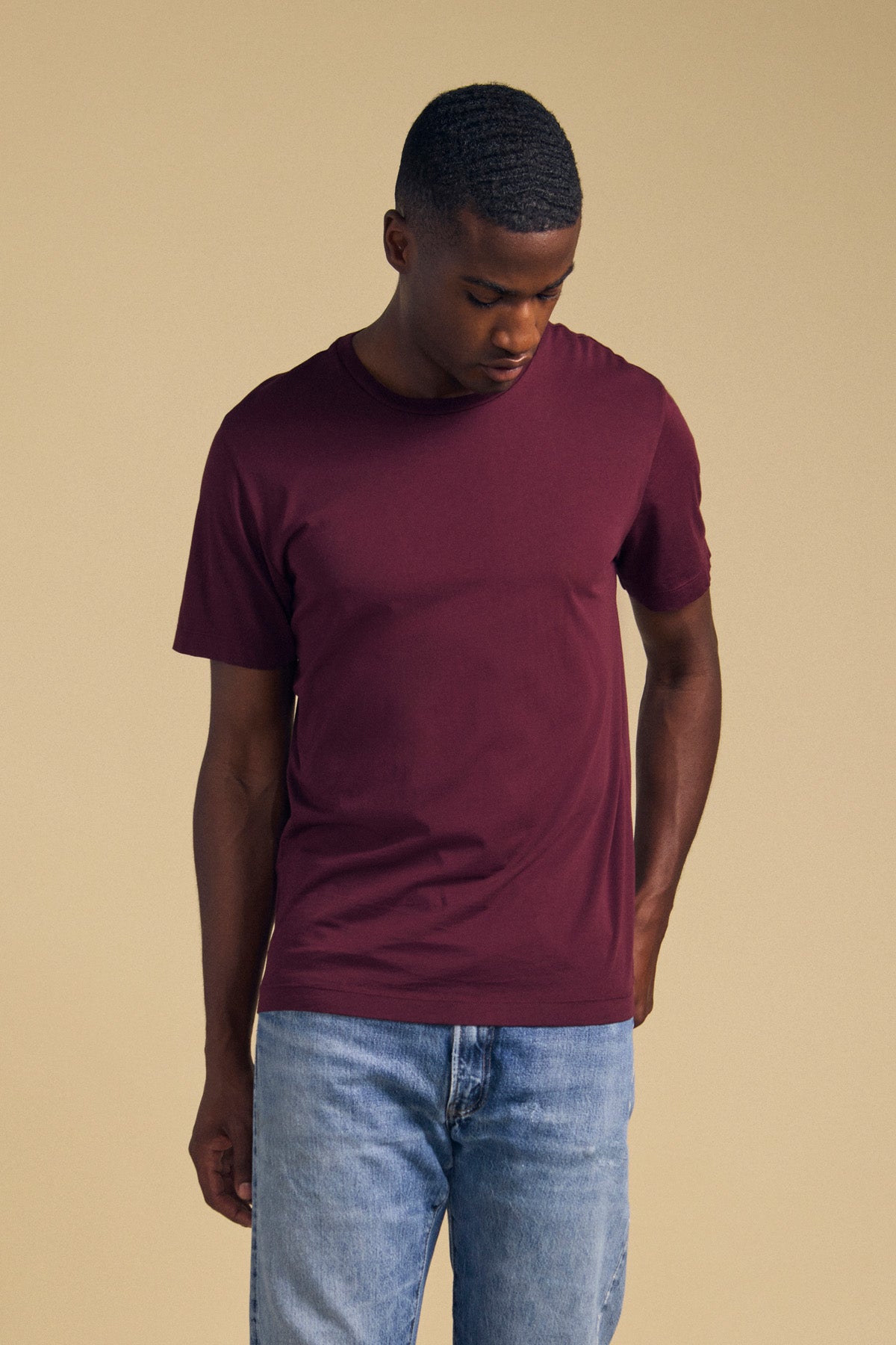 A man wearing blue jeans and a maroon HOWARD TEE, a perfectly fitted Pima jersey crew-neck t-shirt.