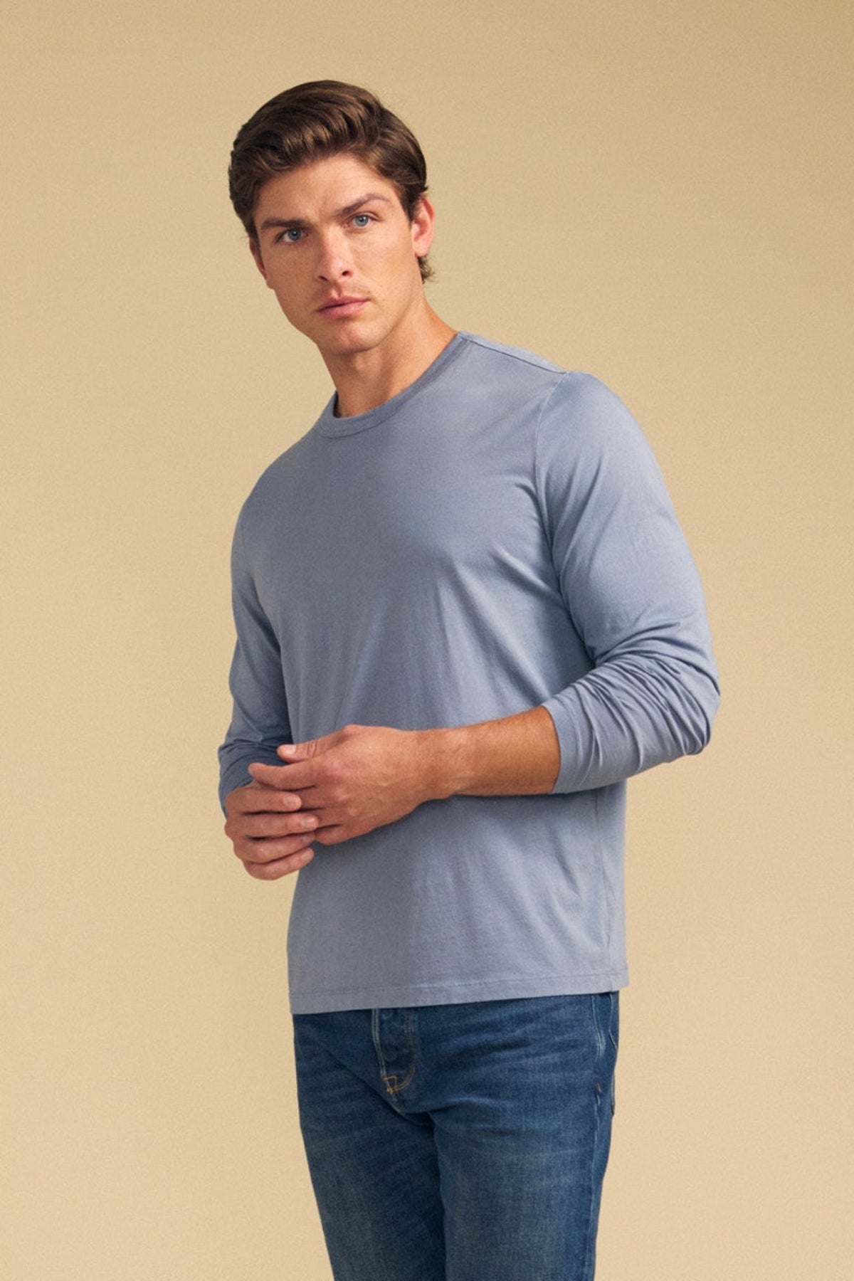 Wearing the ROWLAND TEE by Velvet by Graham & Spencer in light blue and blue jeans, a person stands against a beige background, gazing slightly to the side.-41702119178433