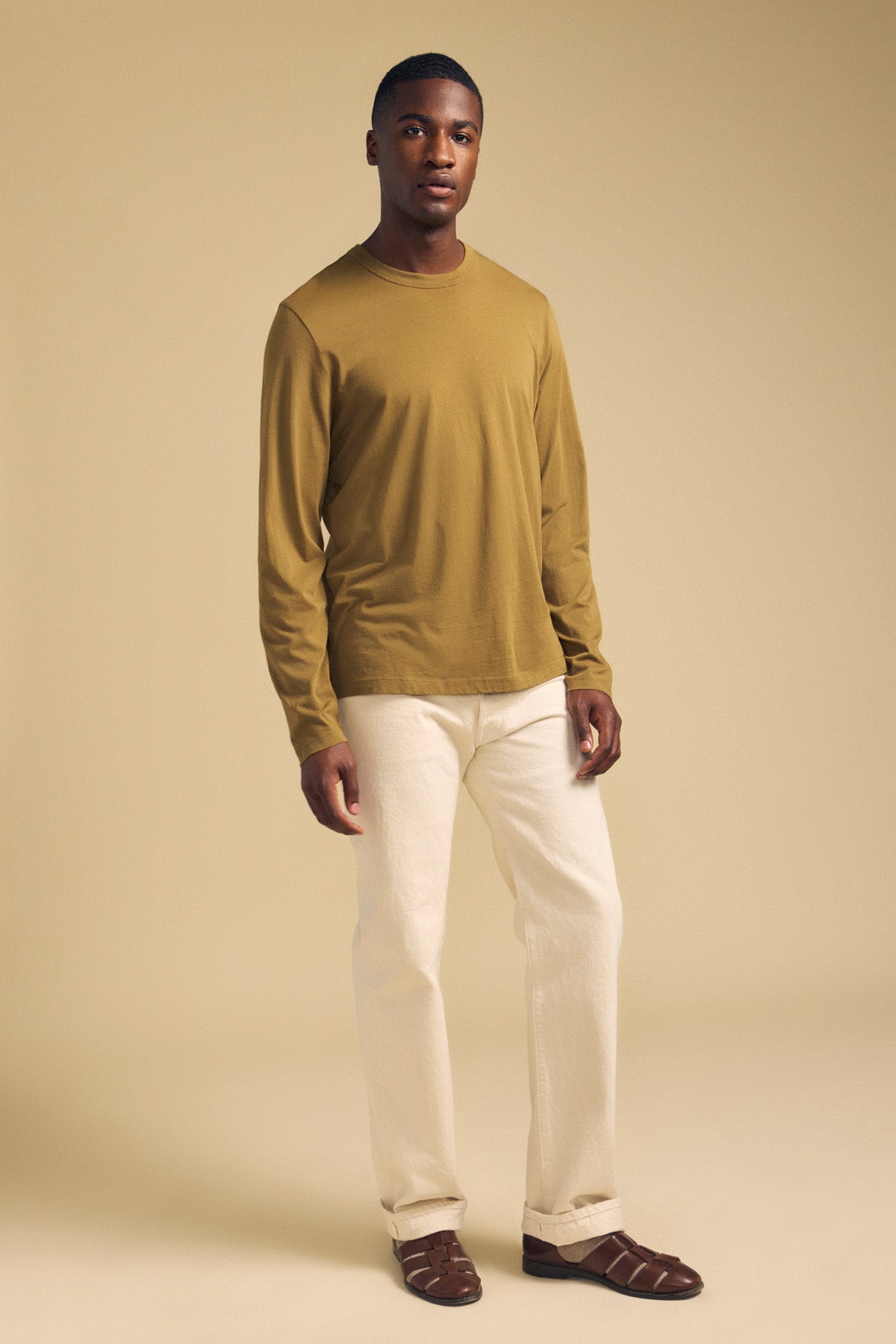 A man wearing an olive ROWLAND TEE long-sleeve crew-neck shirt, off-white trousers, and dark brown leather sandals.-46288297132225