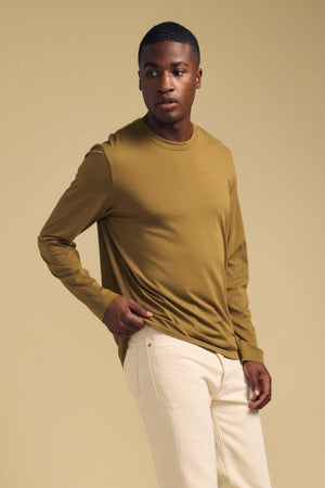 Man wearing an olive green ROWLAND TEE long-sleeve crewneck shirt and light-colored pants.