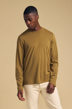A man wearing an olive green long-sleeve ROWLAND TEE by Velvet by Graham & Spencer and white pants.