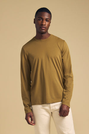 A man wearing an olive green ROWLAND TEE long-sleeve Pima jersey crew-neck t-shirt and white pants.