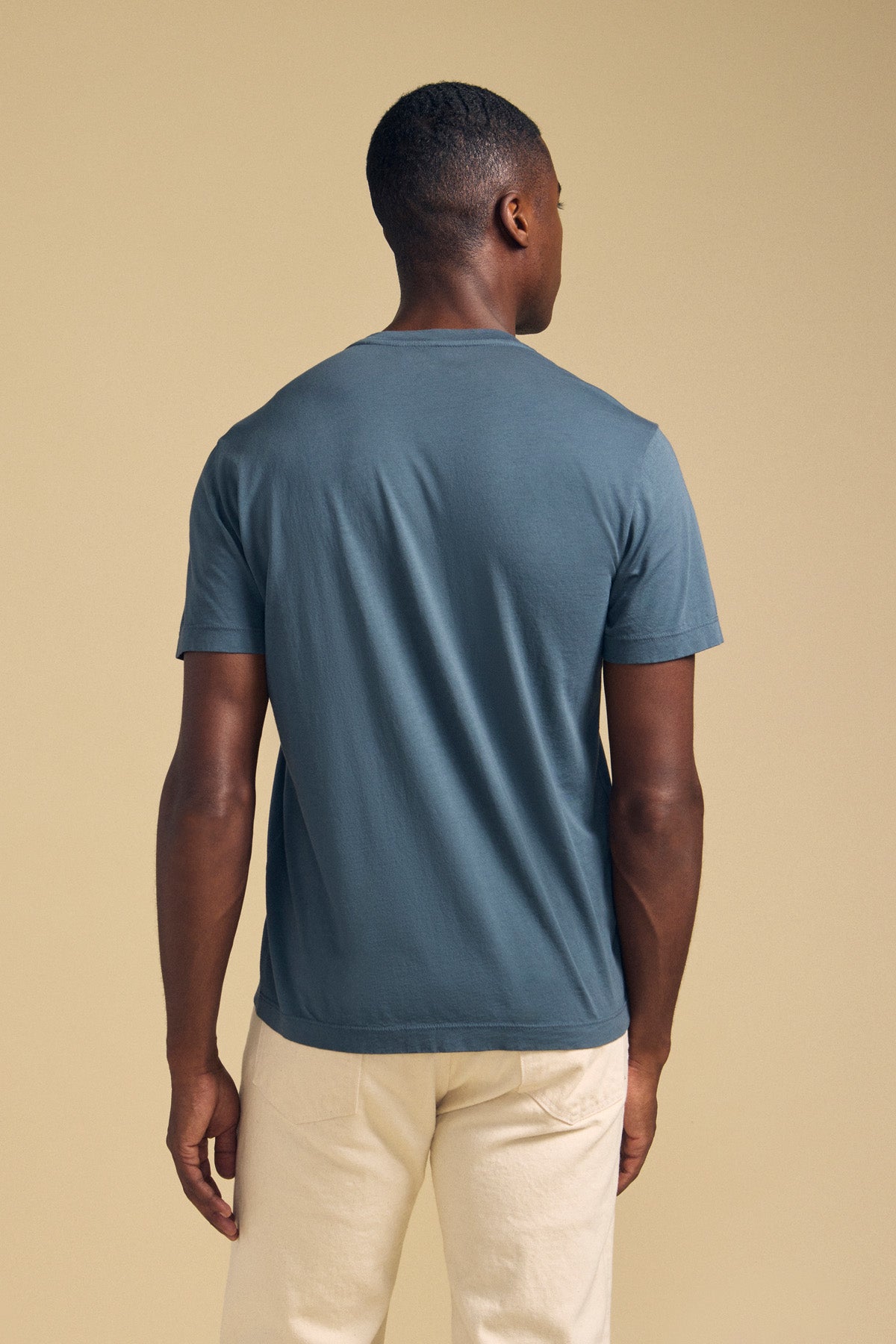 Back view of a person wearing a slate blue SAMSEN TEE Pima jersey crew neck t-shirt and cream-colored pants for everyday wear.-46288454877377