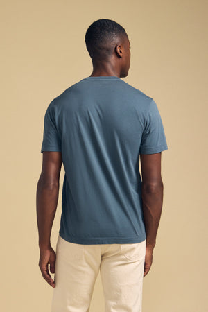 Back view of a person wearing a slate blue SAMSEN TEE Pima jersey crew neck t-shirt and cream-colored pants for everyday wear.