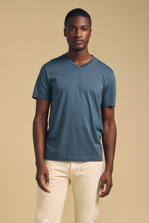 A man wearing a slate blue SAMSEN TEE Pima jersey V-neck T-shirt and cream-colored pants.