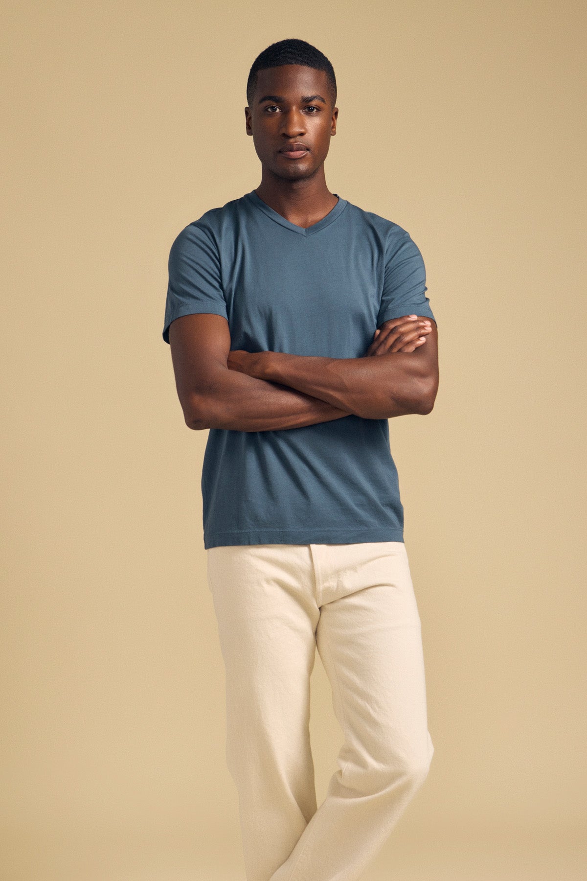 A man with his arms crossed wearing a blue SAMSEN TEE Pima jersey v-neck t-shirt and cream-colored pants.-46288454811841