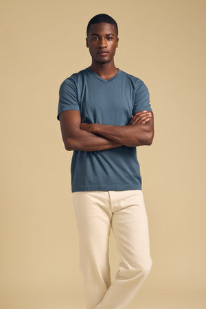 A man with his arms crossed wearing a blue SAMSEN TEE Pima jersey v-neck t-shirt and cream-colored pants.