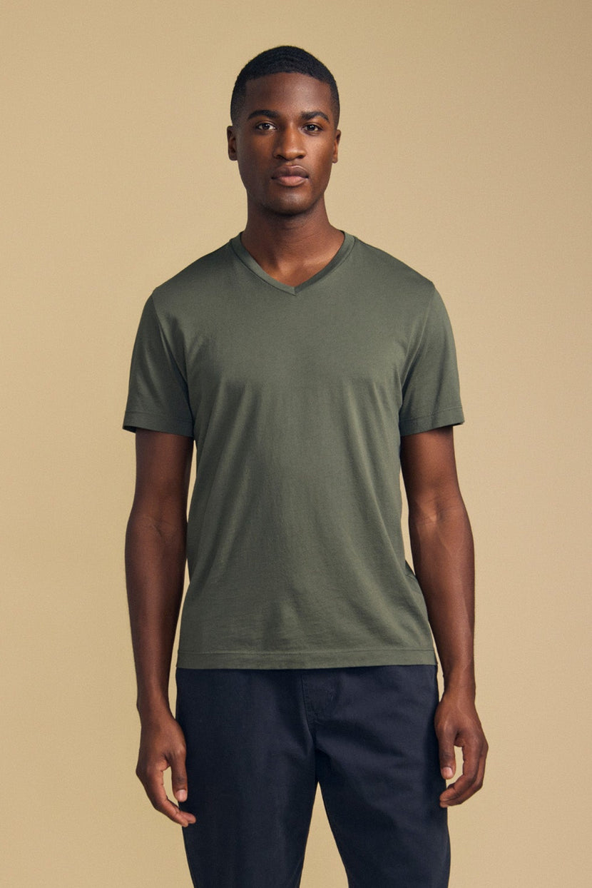 A man stands against a beige background, facing forward with a neutral expression, wearing the Velvet by Graham & Spencer SAMSEN TEE—an olive green V-neck crafted from soft Pima jersey—paired with dark pants; an ideal choice for comfortable everyday wear.