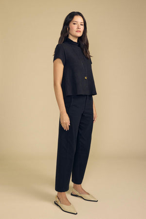 A person wearing a black mock-neck short-sleeve top, matching high-waisted Velvet by Graham & Spencer TENLEY PANT cotton twill pants, and light-colored pointed-toe slingback flats.