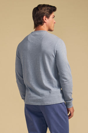 A man faces away, wearing the Velvet by Graham & Spencer ZANE TEE in light blue cotton slub with blue pants, set against a plain beige background.