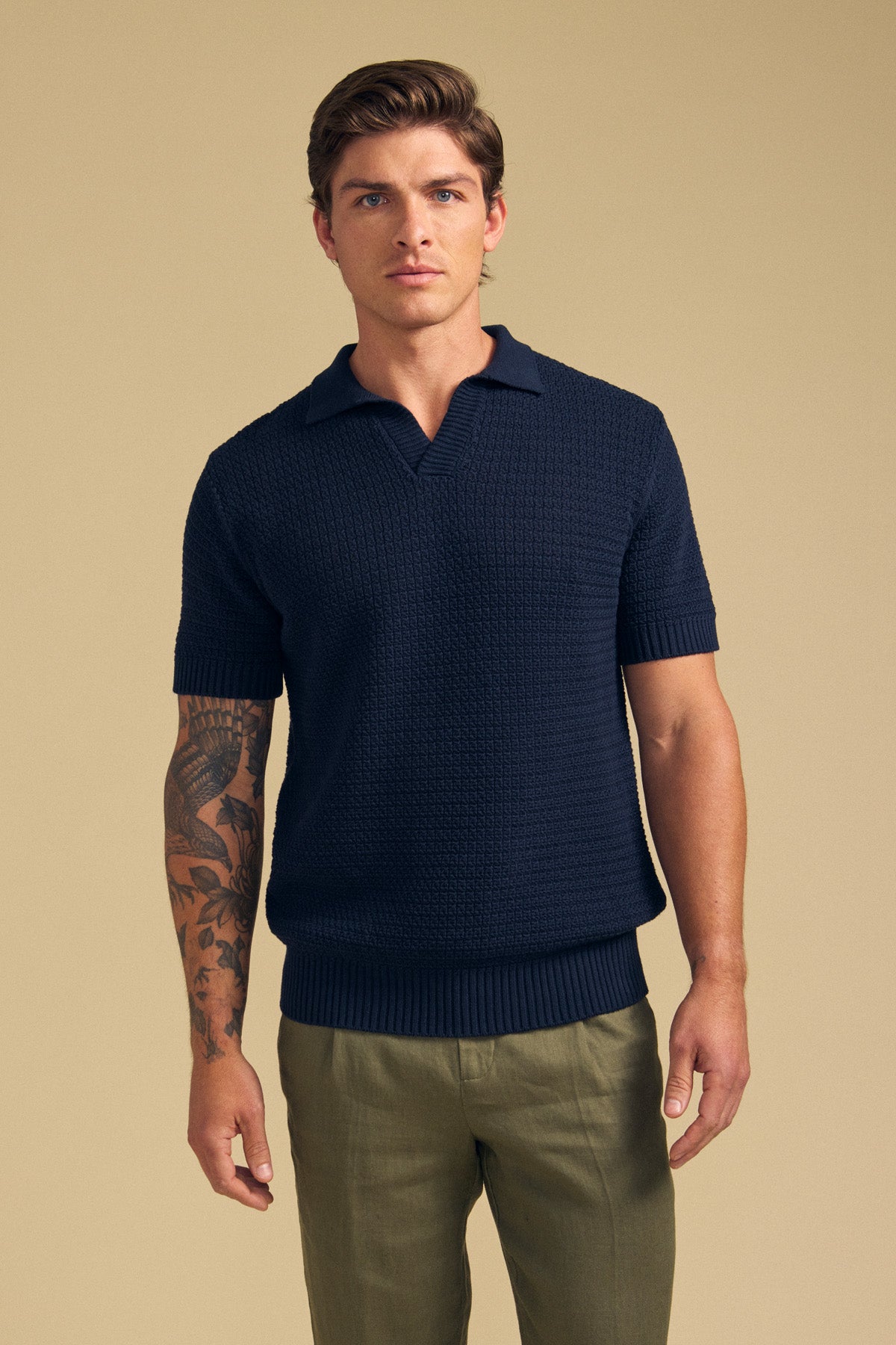 A man with short brown hair wears the CARSTON SWEATER POLO by Velvet by Graham & Spencer and olive green pants, standing against a beige background. One arm features a visible tattoo sleeve.-41701741101249