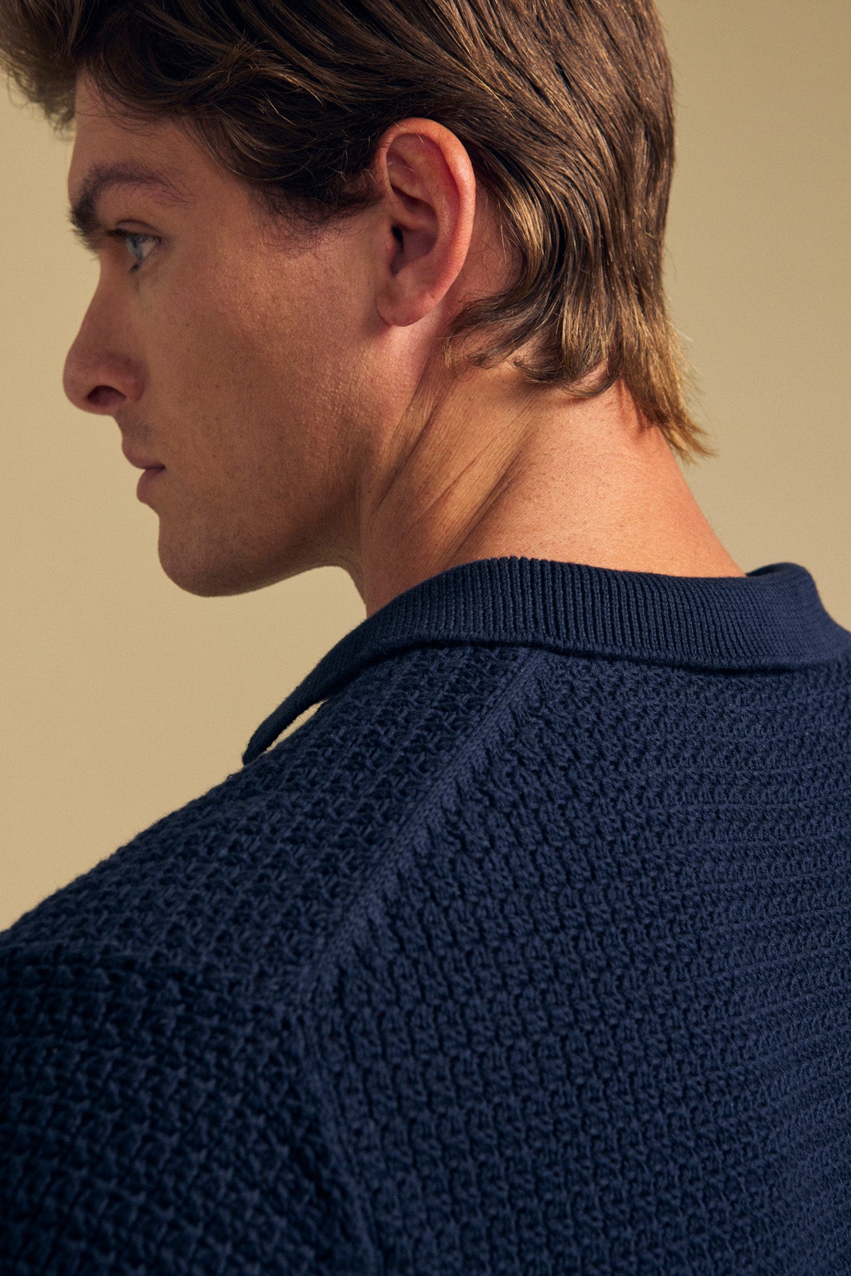 A man with light brown hair is shown in profile, wearing the CARSTON SWEATER POLO by Velvet by Graham & Spencer in navy blue, and looking to the left against a beige background.-41701741068481