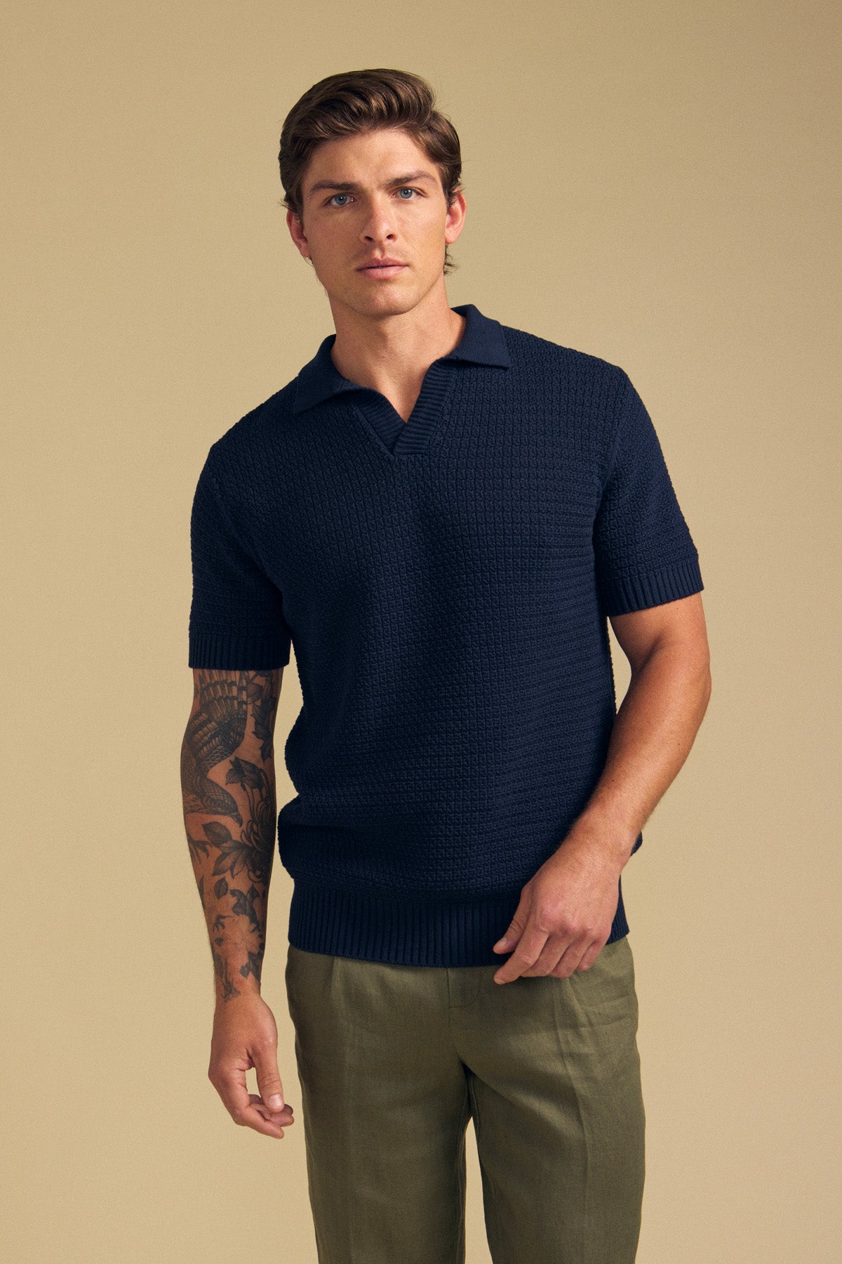 A man with short brown hair wears the Velvet by Graham & Spencer CARSTON SWEATER POLO in navy and olive pants, standing against a beige background.