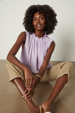 A woman is sitting on the floor in a Velvet by Graham & Spencer BIANCA COTTON GAUZE TANK TOP and tan pants.