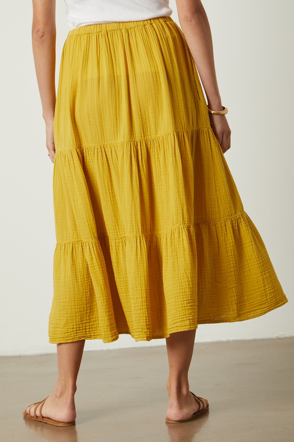 The back view of a woman wearing a yellow Danielle Cotton Gauze Tiered Skirt by Velvet by Graham & Spencer.-35888321462465