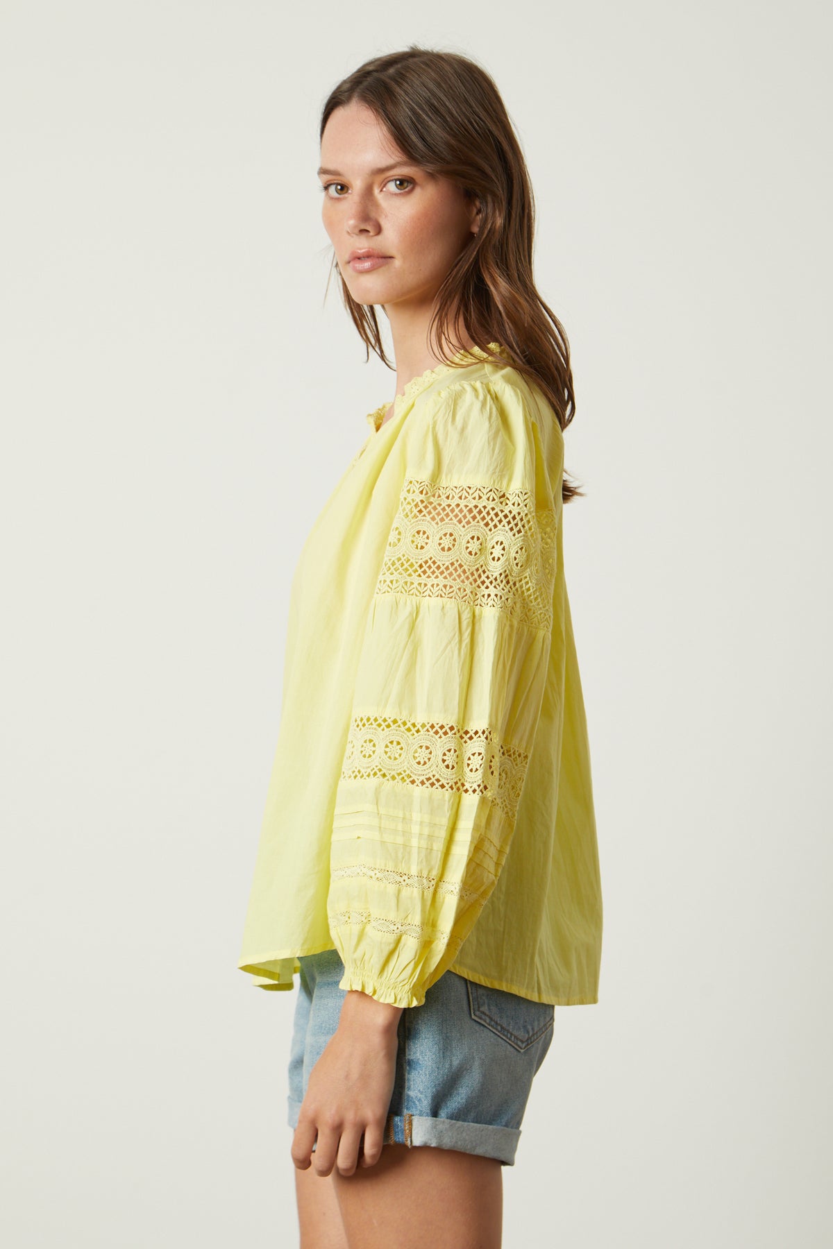 The model is wearing a yellow Velvet by Graham & Spencer blouse with lace sleeves, called the TAYLER COTTON LACE BOHO TOP.-26317098451137
