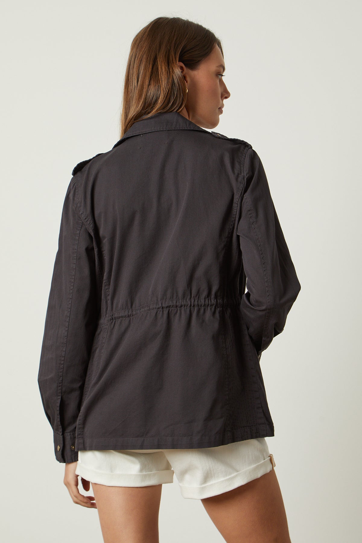 The back view of a woman wearing a Velvet by Graham & Spencer Ruby Light-Weight Army Jacket and white shorts.-26632088027329