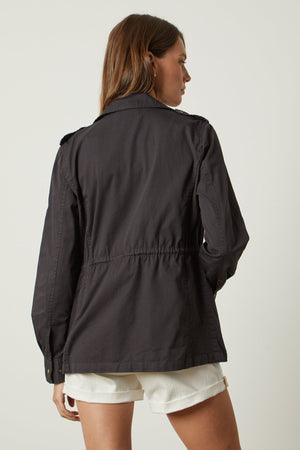 The back view of a woman wearing a Velvet by Graham & Spencer Ruby Light-Weight Army Jacket and white shorts.