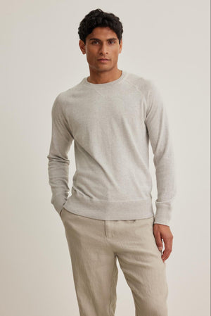 A person stands against a plain background wearing the light gray DARIO COTTON CASHMERE SWEATER by Velvet by Graham & Spencer and beige pants, with hands partially in pockets.