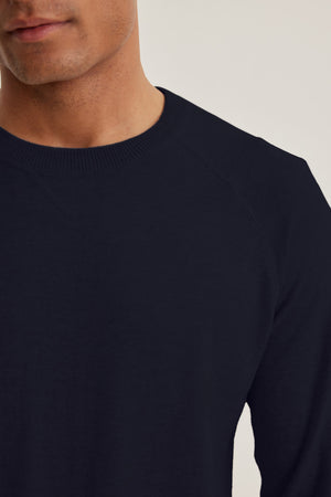 A person wearing the DARIO SWEATER by Velvet by Graham & Spencer, a dark navy mid-weight crewneck, shown from the shoulders up against a neutral background.