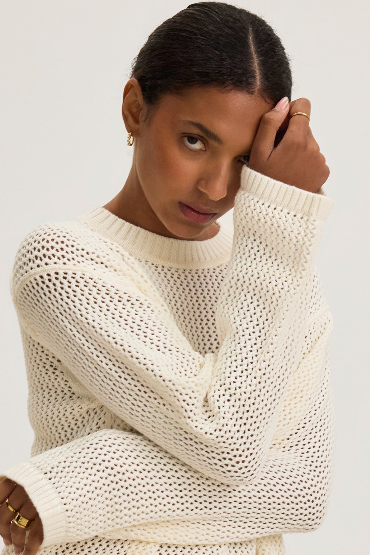 A person is wearing the KANAN COTTON CASHMERE MESH SWEATER by Velvet by Jenny Graham, featuring a white crew neck design, and gazes contemplatively at the camera.-38662760661185