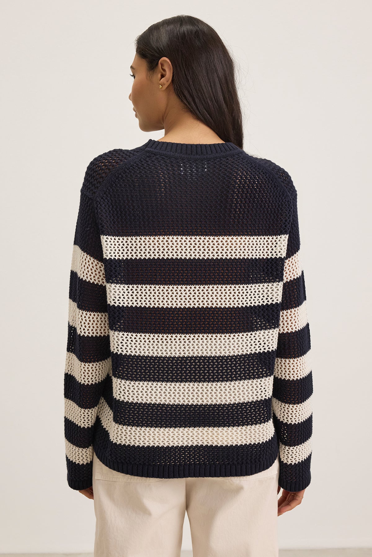   A person with long dark hair is seen from the back, wearing a KANAN COTTON CASHMERE MESH SWEATER by Velvet by Jenny Graham. The sweater is navy and cream striped, made of a soft cotton cashmere blend, with a classic crew neckline, against a plain white background. 