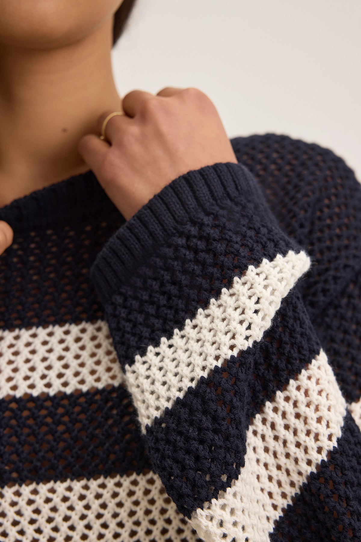   A person wearing the KANAN COTTON CASHMERE MESH SWEATER by Velvet by Jenny Graham with navy and white stripes, adjusts the crew neckline while sporting a gold ring. 