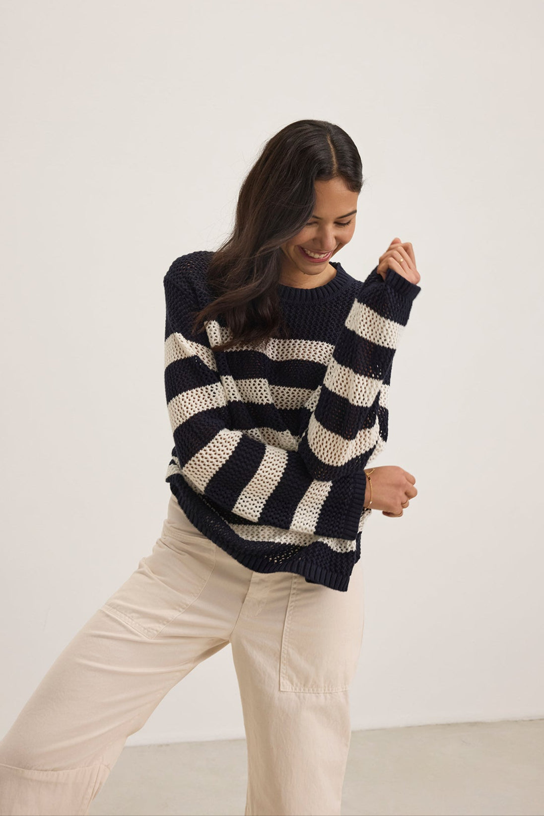   A person in a KANAN COTTON CASHMERE MESH SWEATER by Velvet by Jenny Graham and cream pants stands against a plain background, smiling with eyes closed. 