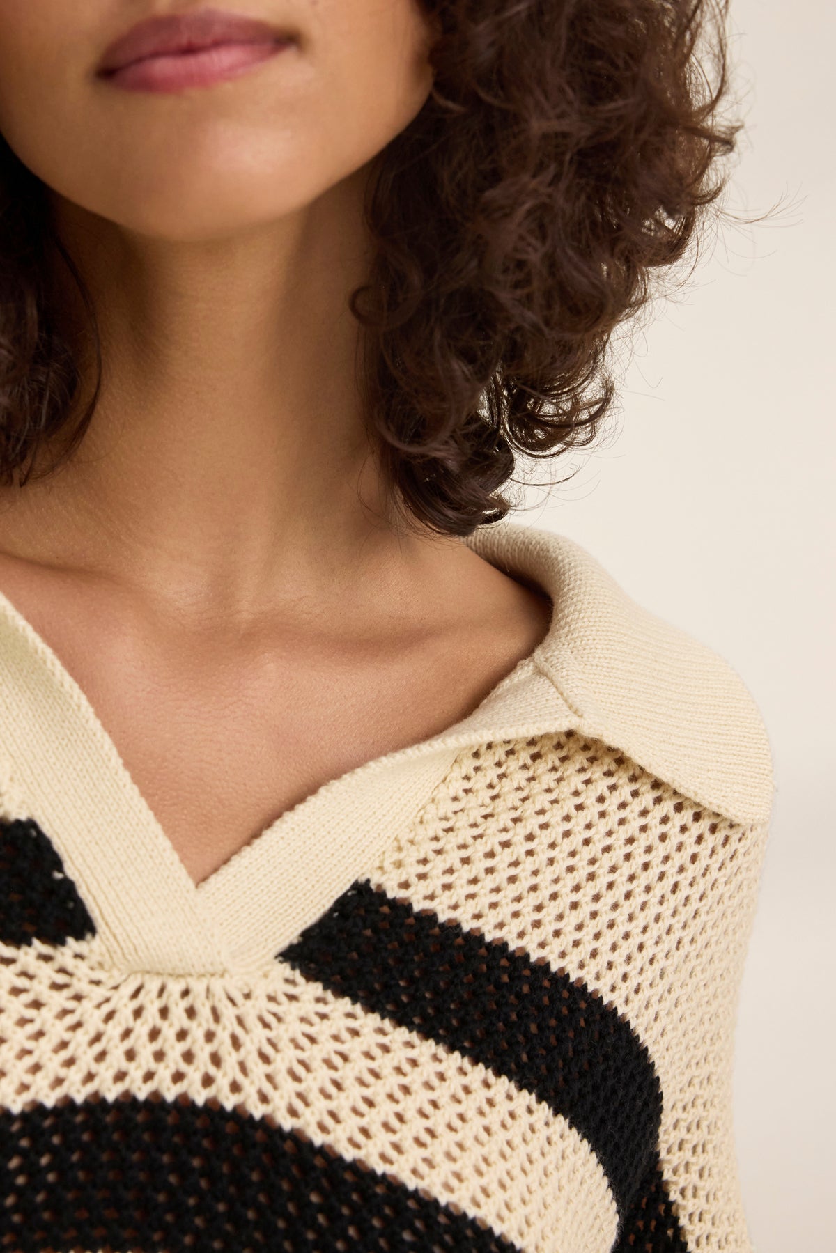 Close-up of a person with curly hair wearing a YORK COTTON CASHMERE MESH SWEATER POLO by Velvet by Jenny Graham, showcasing its polo-style collar and knitted stripes in beige and black.-38928816013505