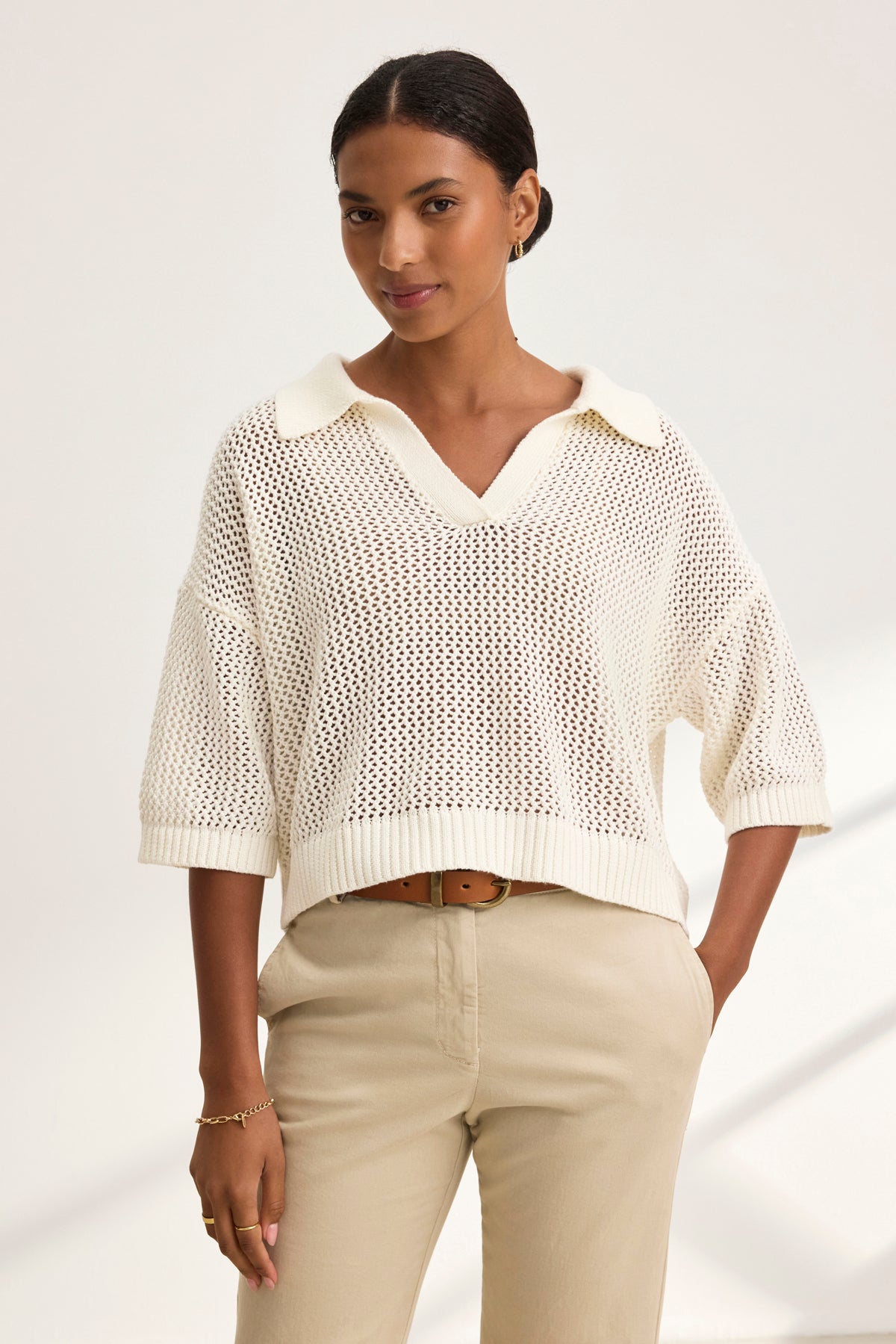 Wearing the YORK COTTON CASHMERE MESH SWEATER POLO from Velvet by Jenny Graham and beige pants, a person stands against a plain background with hands in pockets and a slight smile.-38928816373953